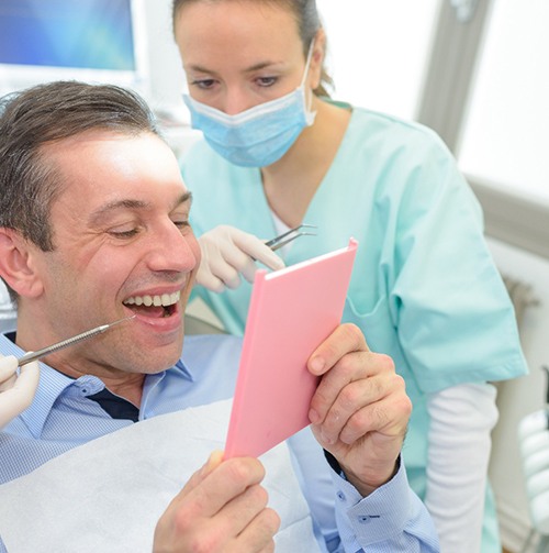 Man in dental chair smiling at his reflection with dentist looking over his shoulder