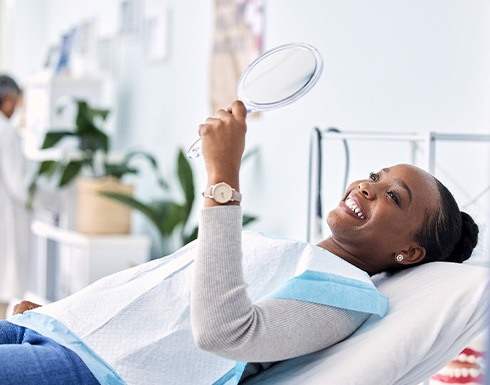 Woman smiling at reflection in handheld mirror