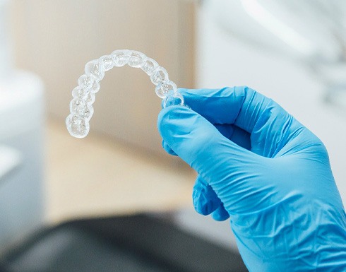 Dentist with blue glove holding clear aligner