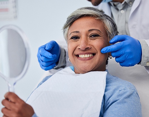 Woman with gray hair smiling while holding mirror