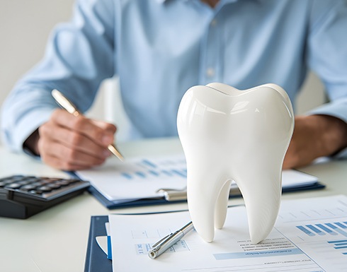 Man calculating costs at desk next to large model tooth
