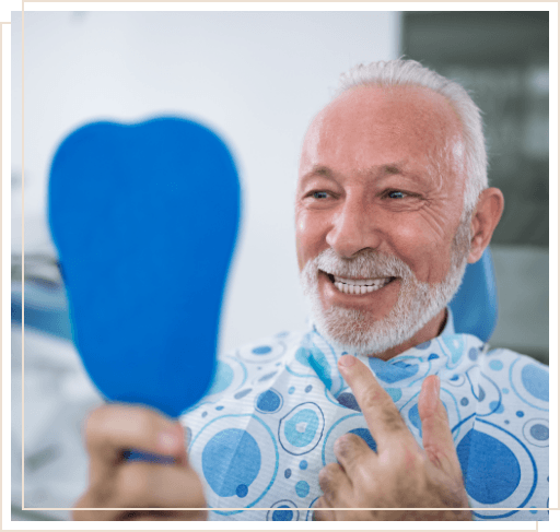 Senior dental patient pointing to his smile while looking in mirror