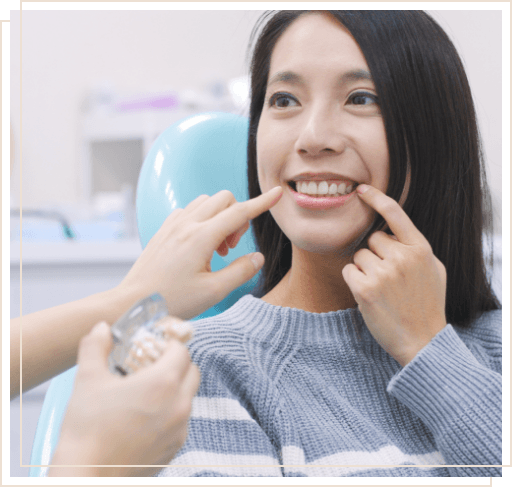 Woman in dental chair pointing to her smile