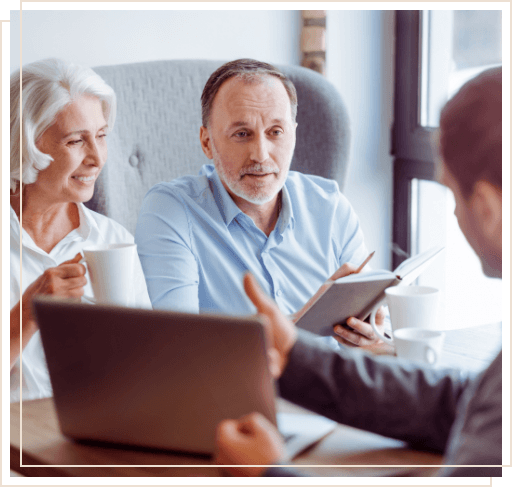 Man showing laptop to two people sitting across desk