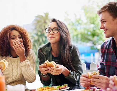 Group of friends smiling while eating food outside