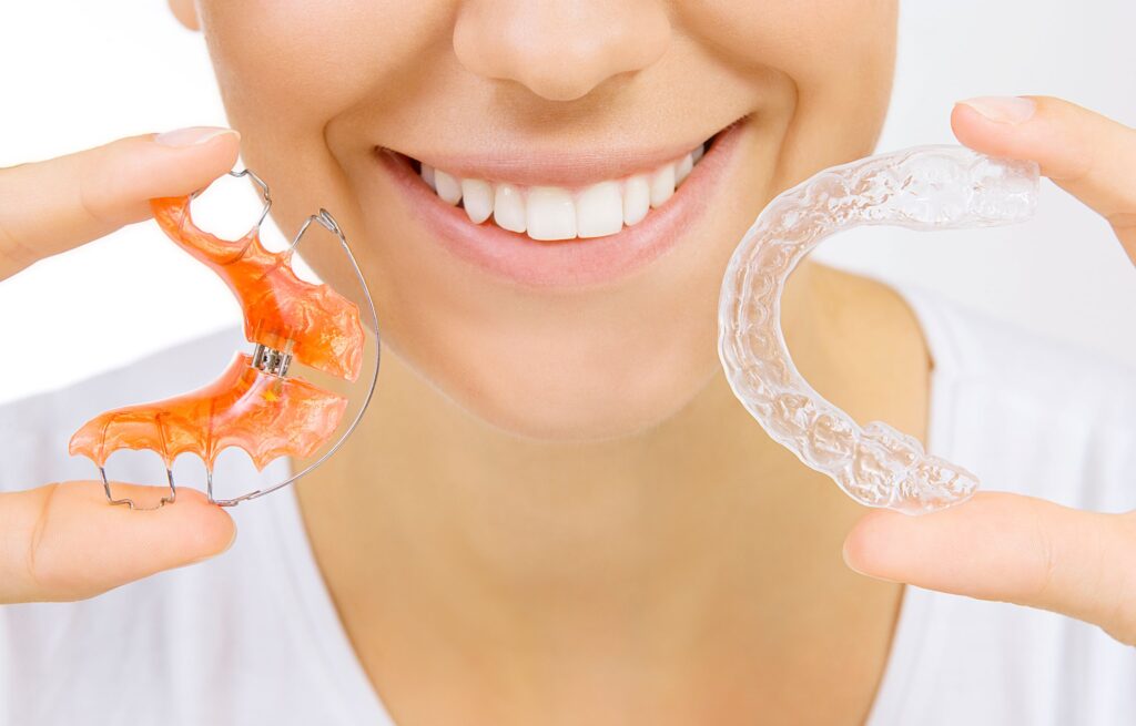 Nose-to-shoulder view of woman holding retainer and clear aligner